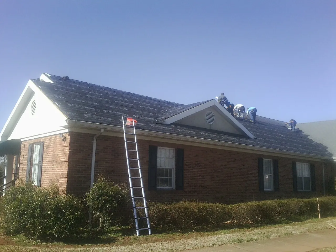 Crew tearing shingles off a brick ranch roof with a ladder set — Metal Roof Repair work by our crew in North Yarmouth