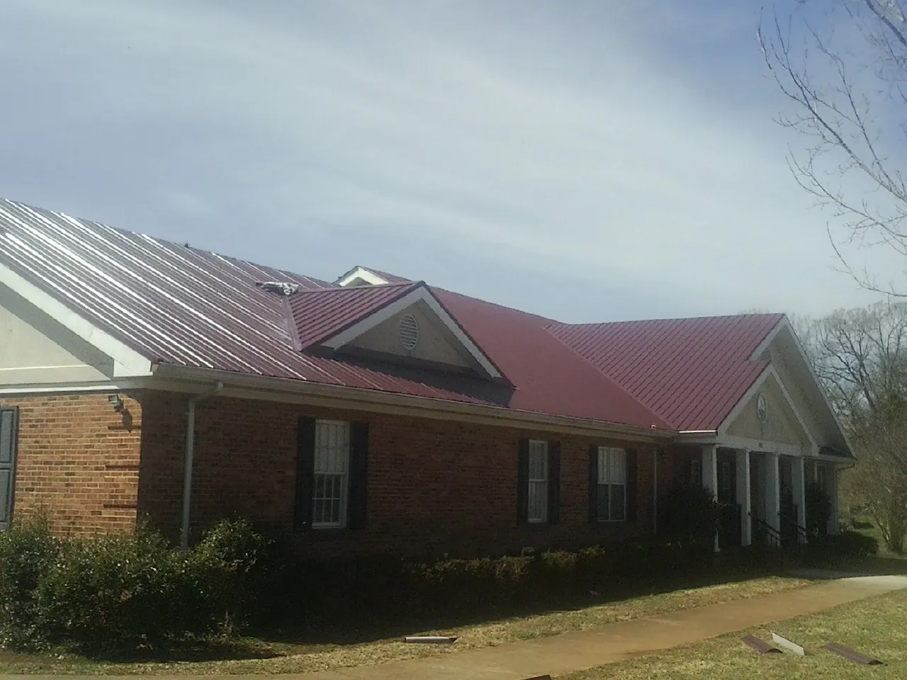 Red metal roof with gabled entries on a long brick building, from a Hail Damage Roof Repair job in North Yarmouth