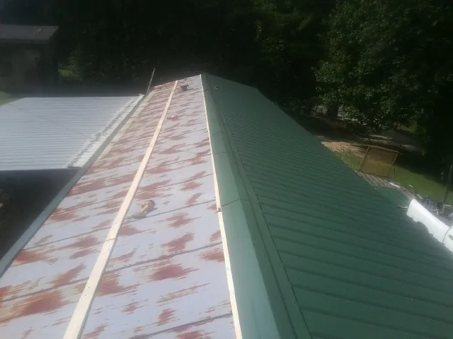 Old rusted panels beside newly installed green metal roofing — Wind Damage Roof Repair by Roofing Brothers in North Yarmouth
