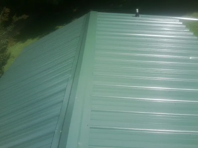 New green metal panels meeting at the ridge of a roof — Flat Roof Repair work by our crew in North Yarmouth