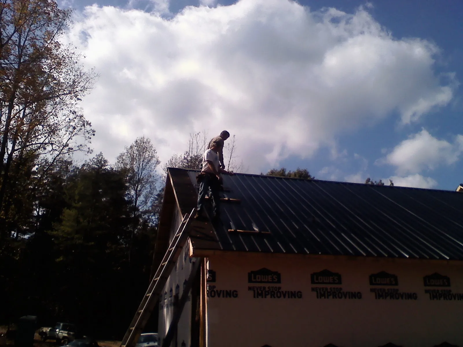 Roofer fastening dark metal panels high against a cloudy sky, from a Roof Inspection job in North Yarmouth