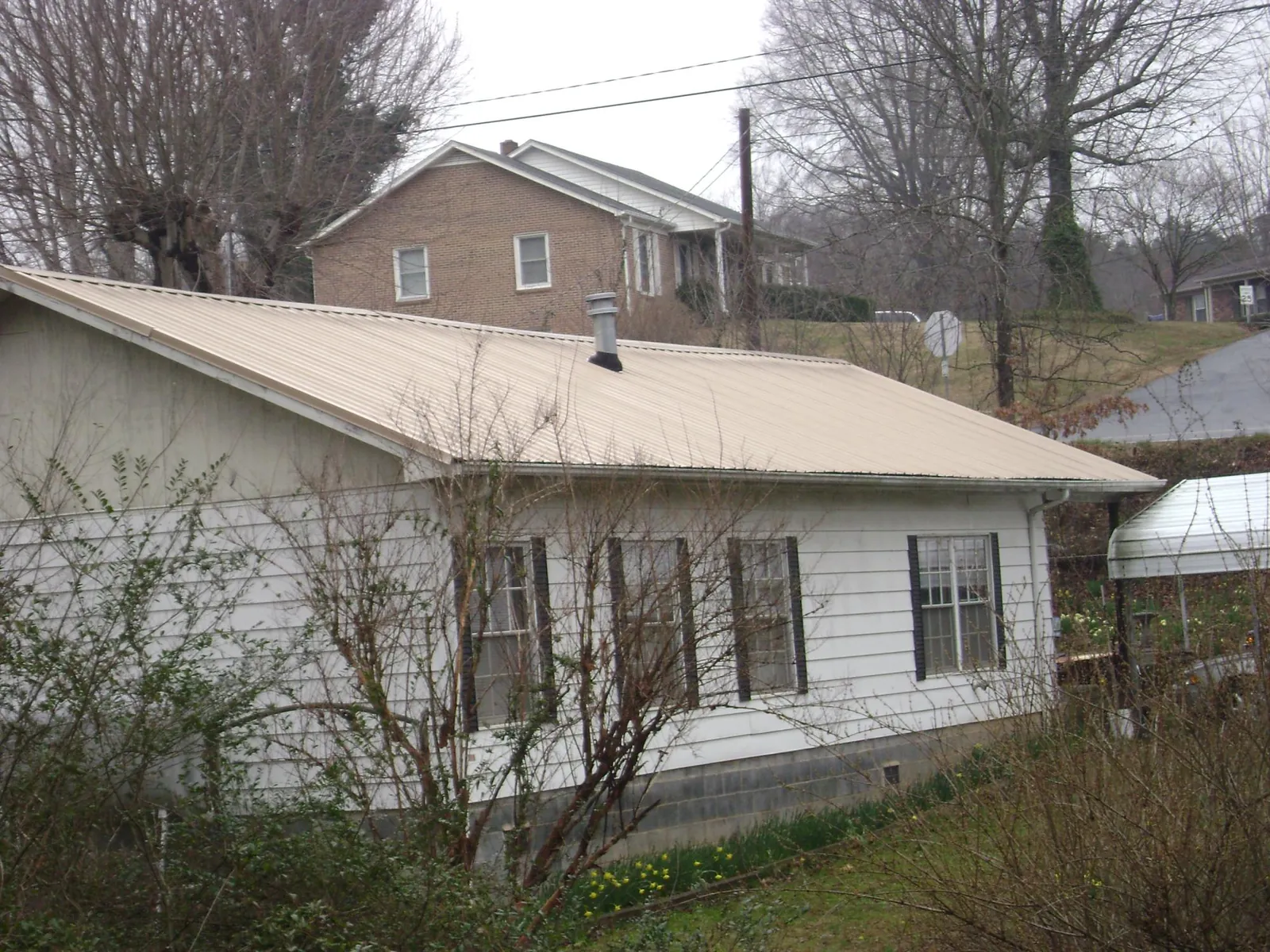 Tan metal roof on a white sided house set into a hillside — Commercial Roofing by Roofing Brothers in North Yarmouth