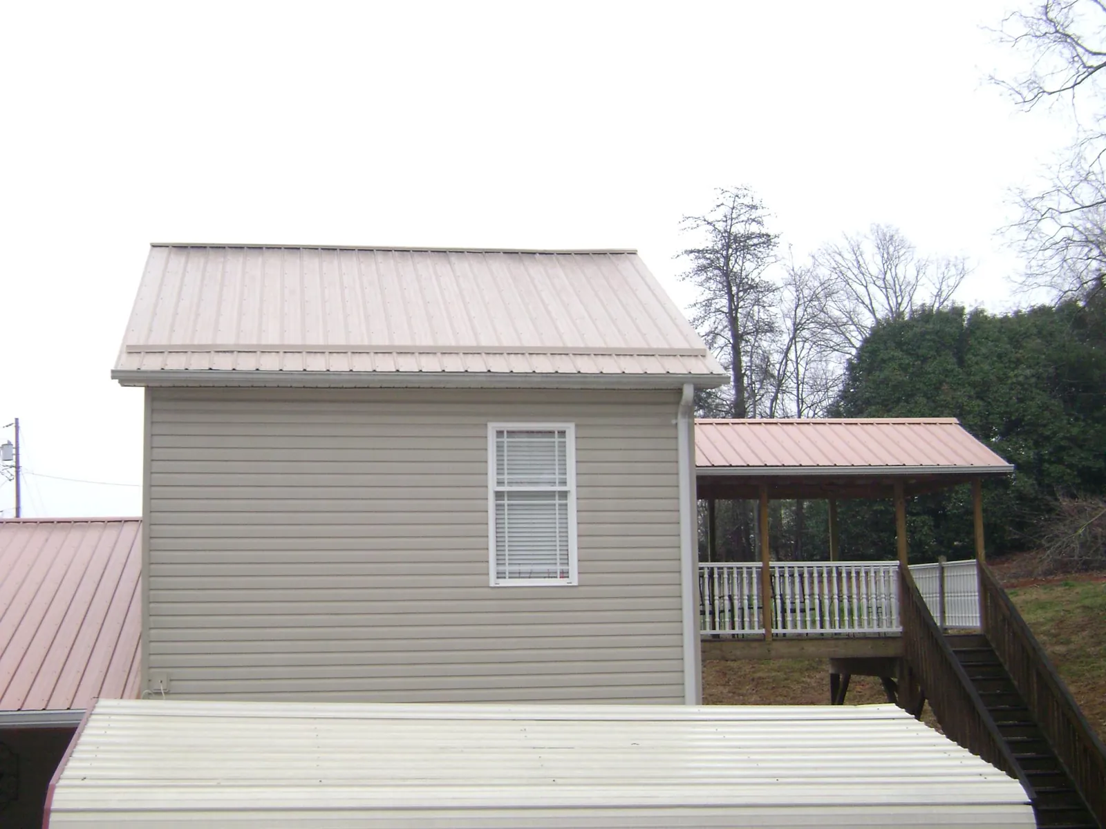 Tan metal roofs on a two story addition and attached porch, from a Roof Replacement job in North Yarmouth